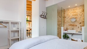 A bedroom with a bed, a wardrobe, a bathroom with a sink and mirror, and a view of a dining area.