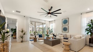 Ein geräumiges Wohnzimmer mit Deckenventilator, großem Fenster und Blick ins Freie.