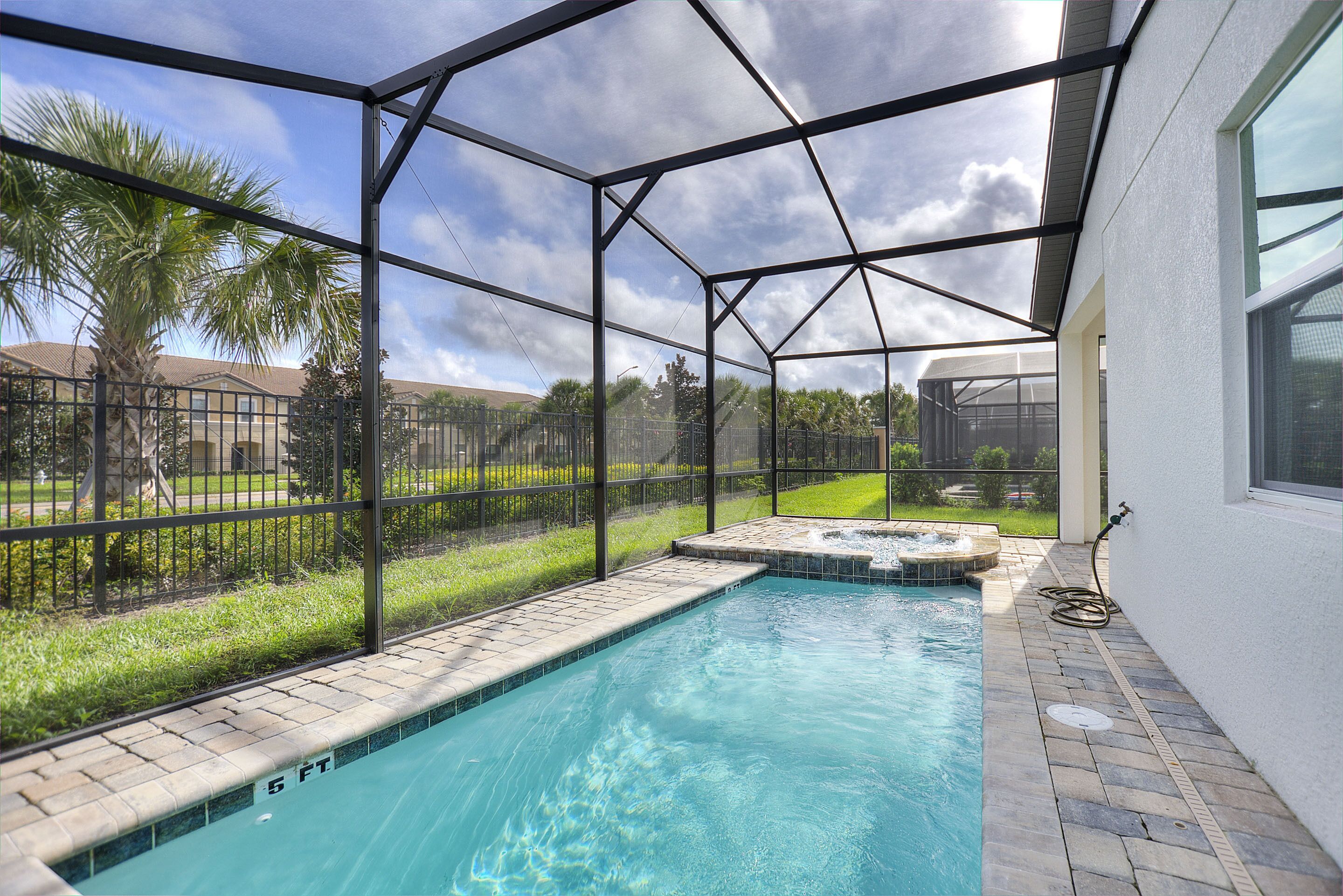 A swimming pool with a clear blue water, surrounded by a glass enclosure, and a hot tub area.