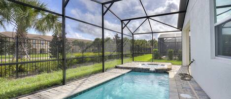 A swimming pool with a clear blue water, surrounded by a glass enclosure, and a hot tub area.