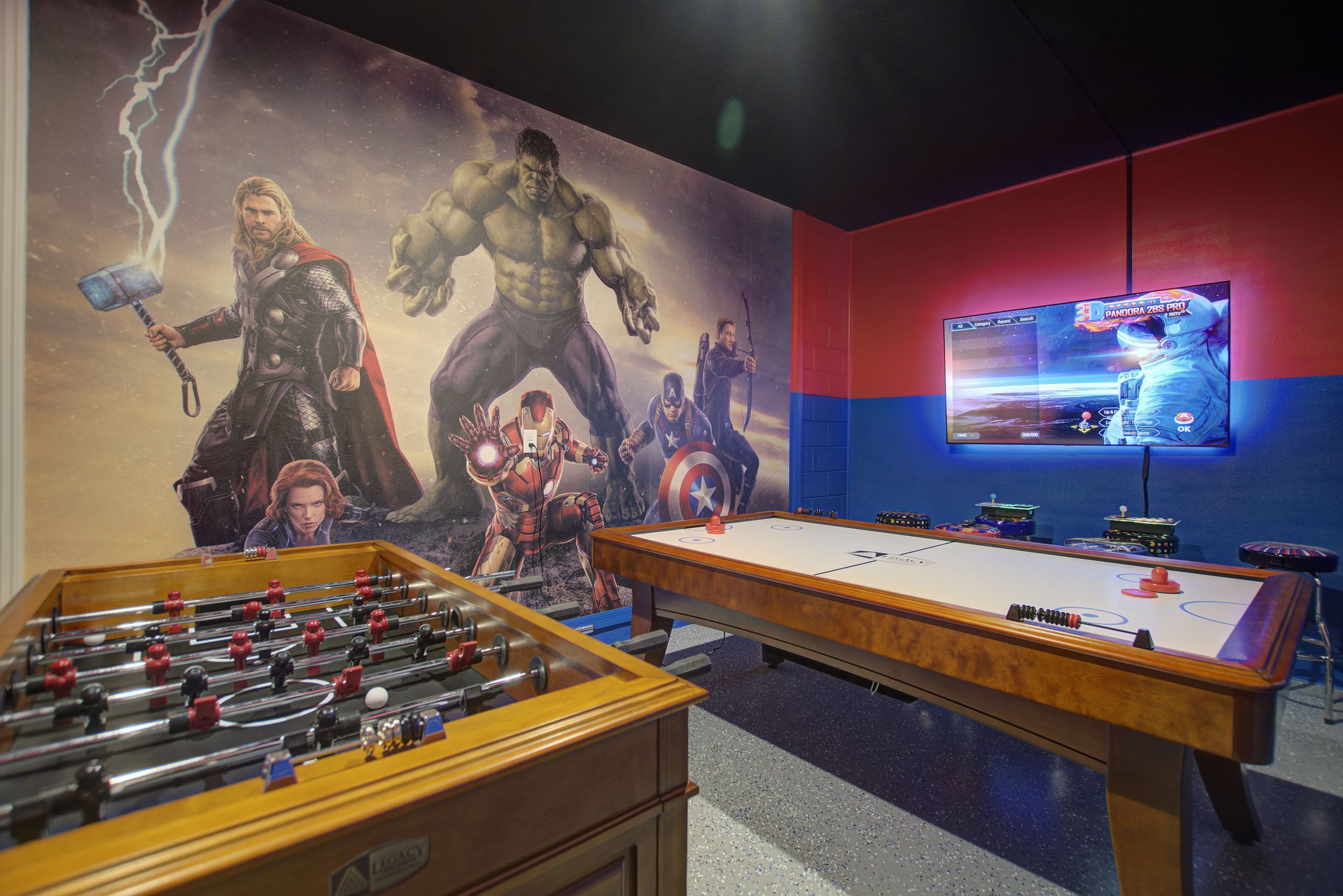 A room with a foosball table, a pool table, and a TV displaying a video game.