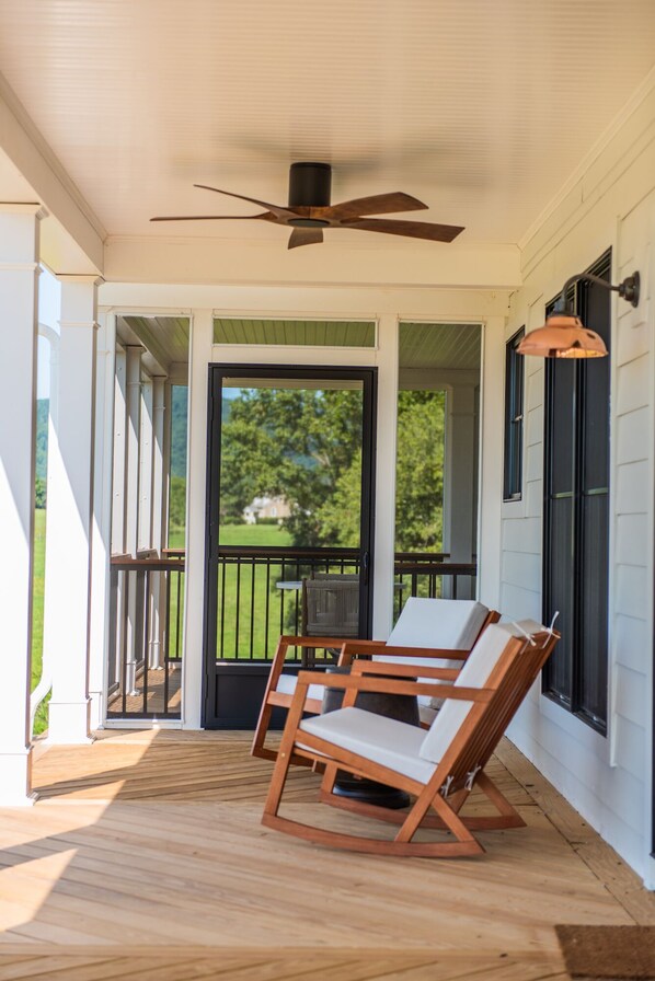 A covered porch with a ceiling fan, wooden deck, and two rocking chairs. - The Farmhouse at Blue Rock (Washington)