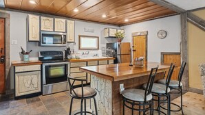 A kitchen with a central island, bar stools, a microwave, stove, refrigerator, and wooden cabinets. - Chickahominy Riverside Guest Home 30 Minutes to Williamsburg! (Charles City)
