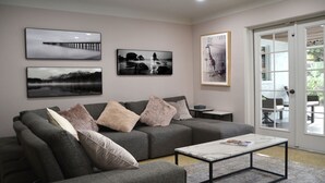 A modern living room with a grey sofa, a coffee table, and three framed pictures on the wall. - Arlington Park Area! 3BR/2BA Sarasota Home – Heated Large Pool (Sarasota)