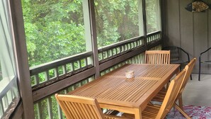 A wooden deck with a table and chairs, surrounded by large windows offering a view of greenery. - Lovely Bluewater Bay 1 Bedroom Condo near Bluewater Bay Marina and Destin Island (Niceville)