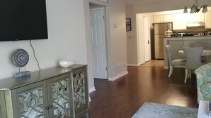 A living room with a TV, a cabinet, and a dining area with chairs and a table. - Lovely Bluewater Bay 1 Bedroom Condo near Bluewater Bay Marina and Destin Island (Niceville)