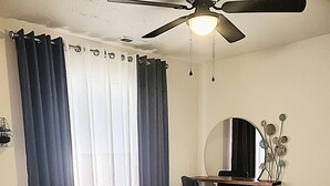A bedroom with a bed, a ceiling fan, a mirror, and a window with curtains. - Sunset Hills1600 sq. ft. lower-level apt.<br>(3 bedrooms, 2 king beds) (Nampa)