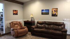 Un salon avec un canapé en cuir marron et un fauteuil en cuir marron, une lampe sur une table d’appoint et trois tableaux accrochés au mur.
