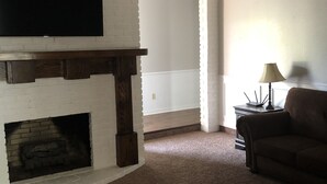 Un salon doté d’une cheminée, d’un ventilateur de plafond, d’un téléviseur à écran plat fixé à un mur en briques et d’un canapé marron.