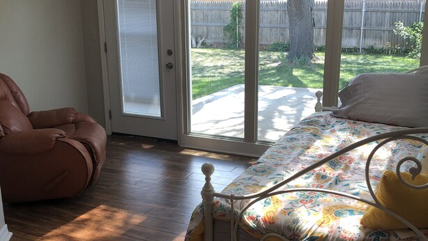 Une chambre à coucher avec un lit, un fauteuil en cuir marron et une porte-fenêtre coulissante donnant sur un jardin.