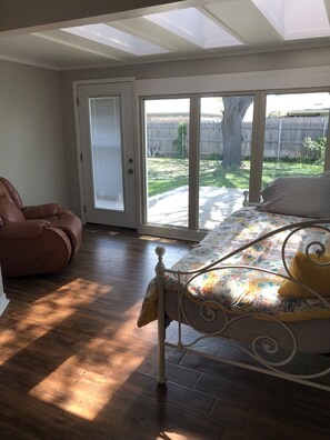 A bedroom with a bed, a brown leather chair, and a sliding glass door leading to a backyard.
