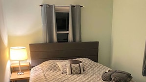 Ein Schlafzimmer mit einem Bett, einem Nachttisch mit Lampe, einem Deckenventilator und einem Fenster mit Vorhängen.