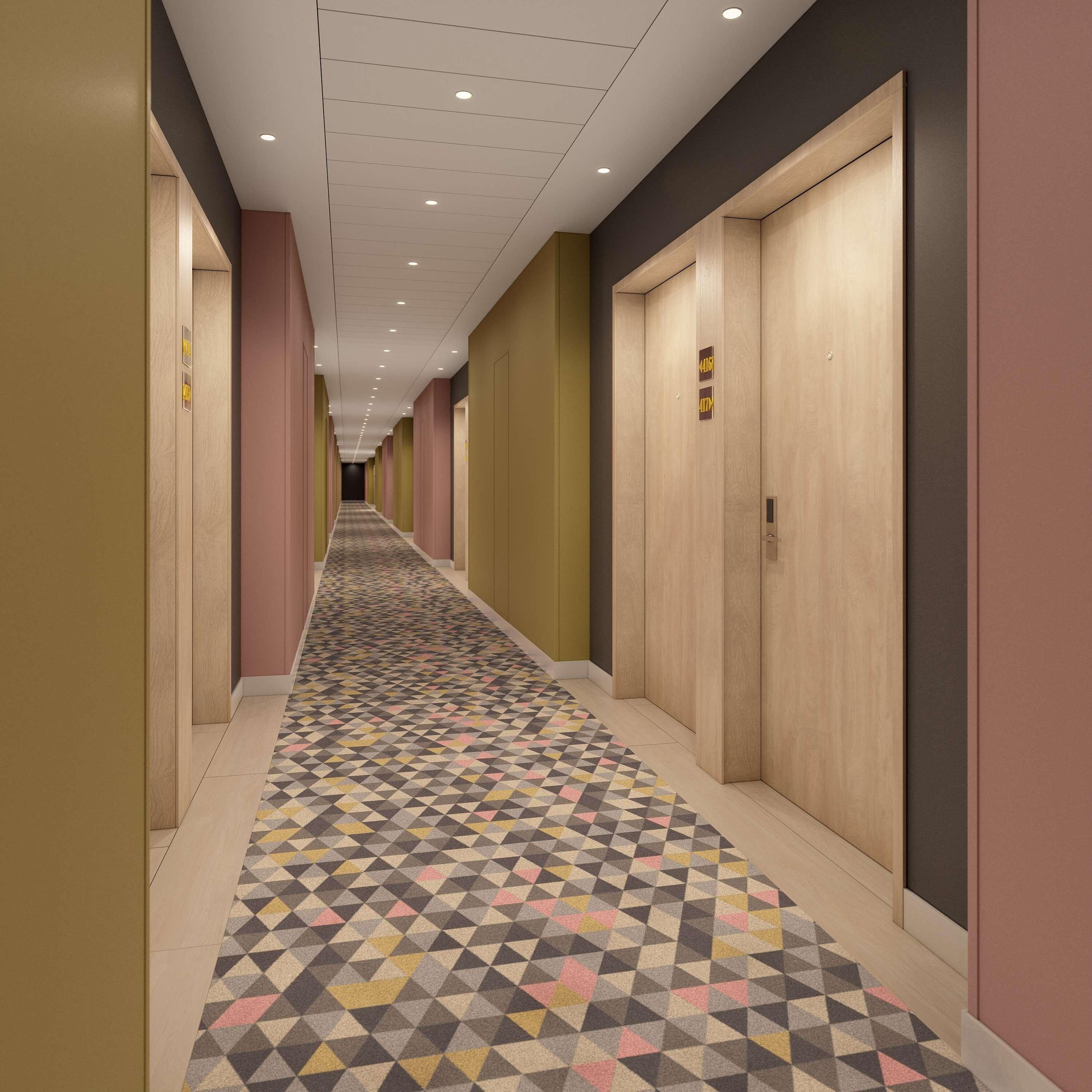 Um corredor de hotel com carpete estampado, portas de madeira e teto com iluminação embutida.