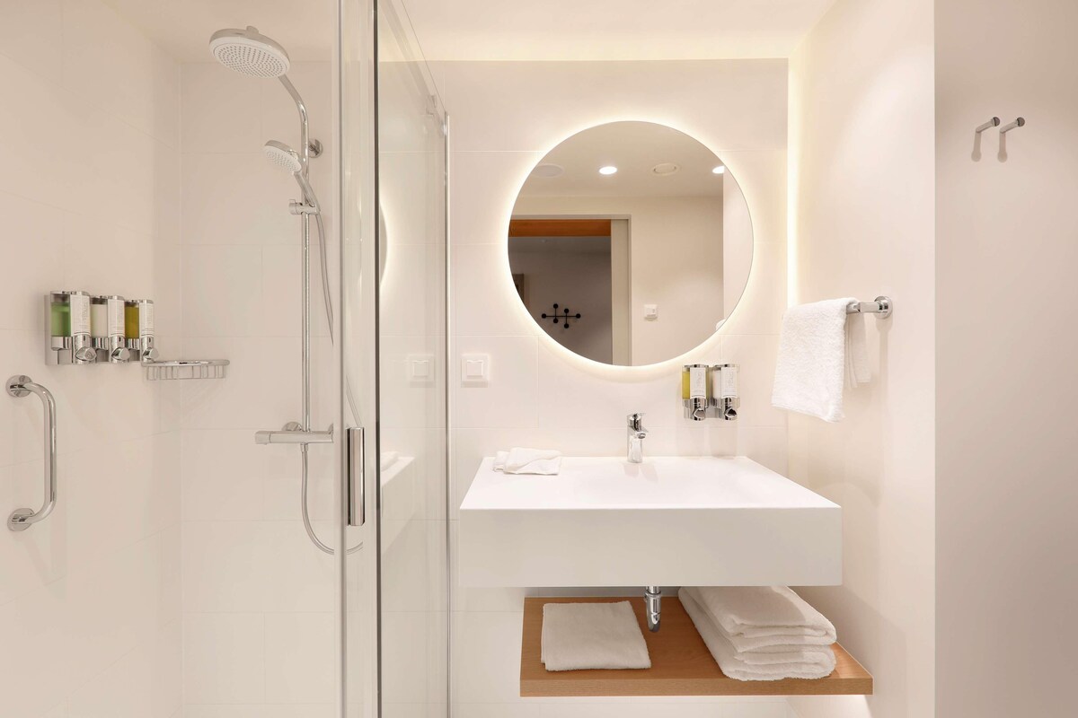 A modern bathroom with a glass-enclosed shower, a white sink with a mirror, and a towel rack.