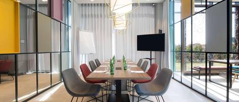 A modern conference room with a long table, multiple chairs, a large screen, and a unique geometric pendant light.