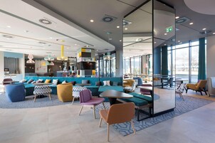 Un moderno espacio de salón con arreglos de asientos, una cocina al fondo y grandes ventanales que ofrecen luz natural.