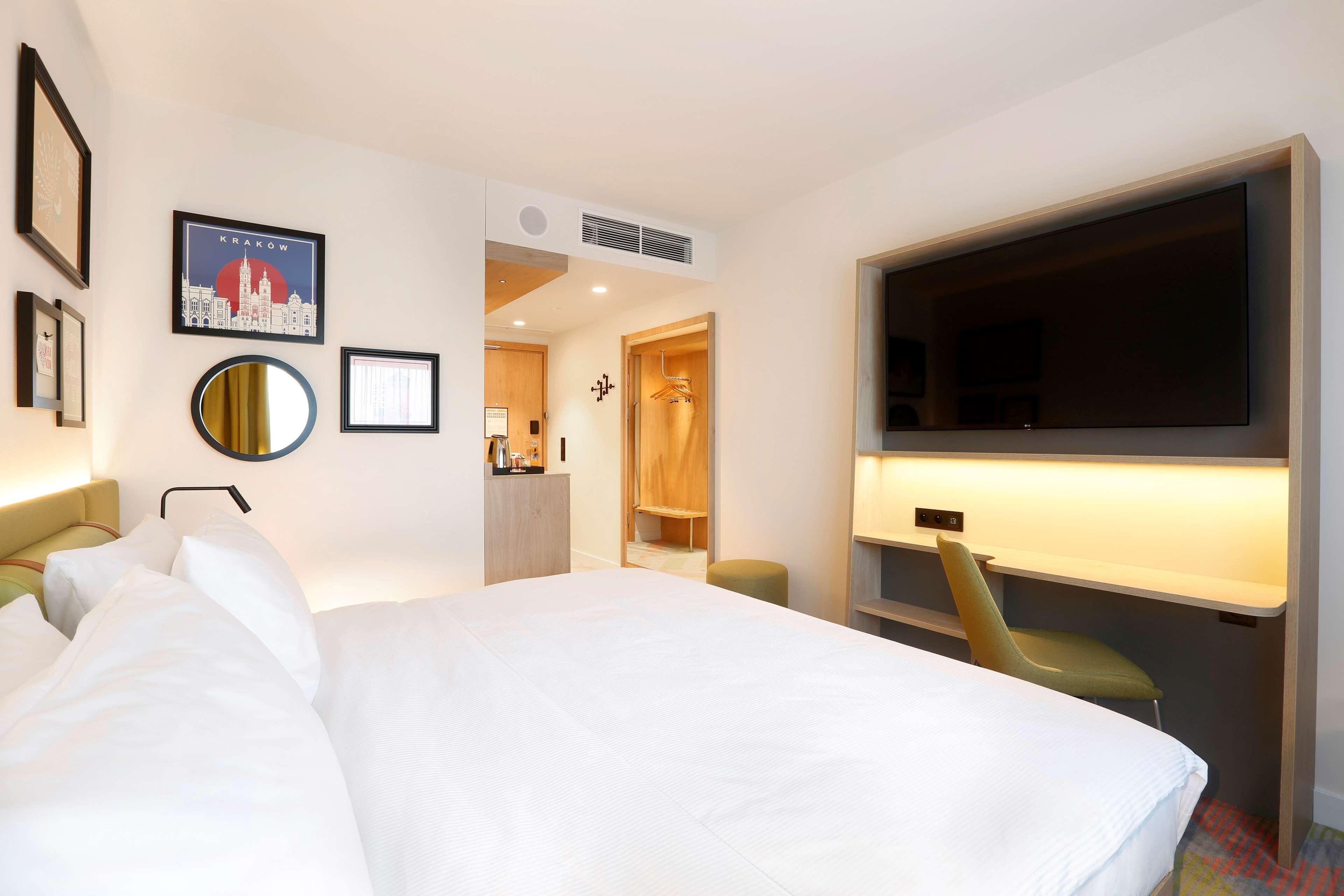 A hotel room with a large bed, a TV, a desk, and a wardrobe.