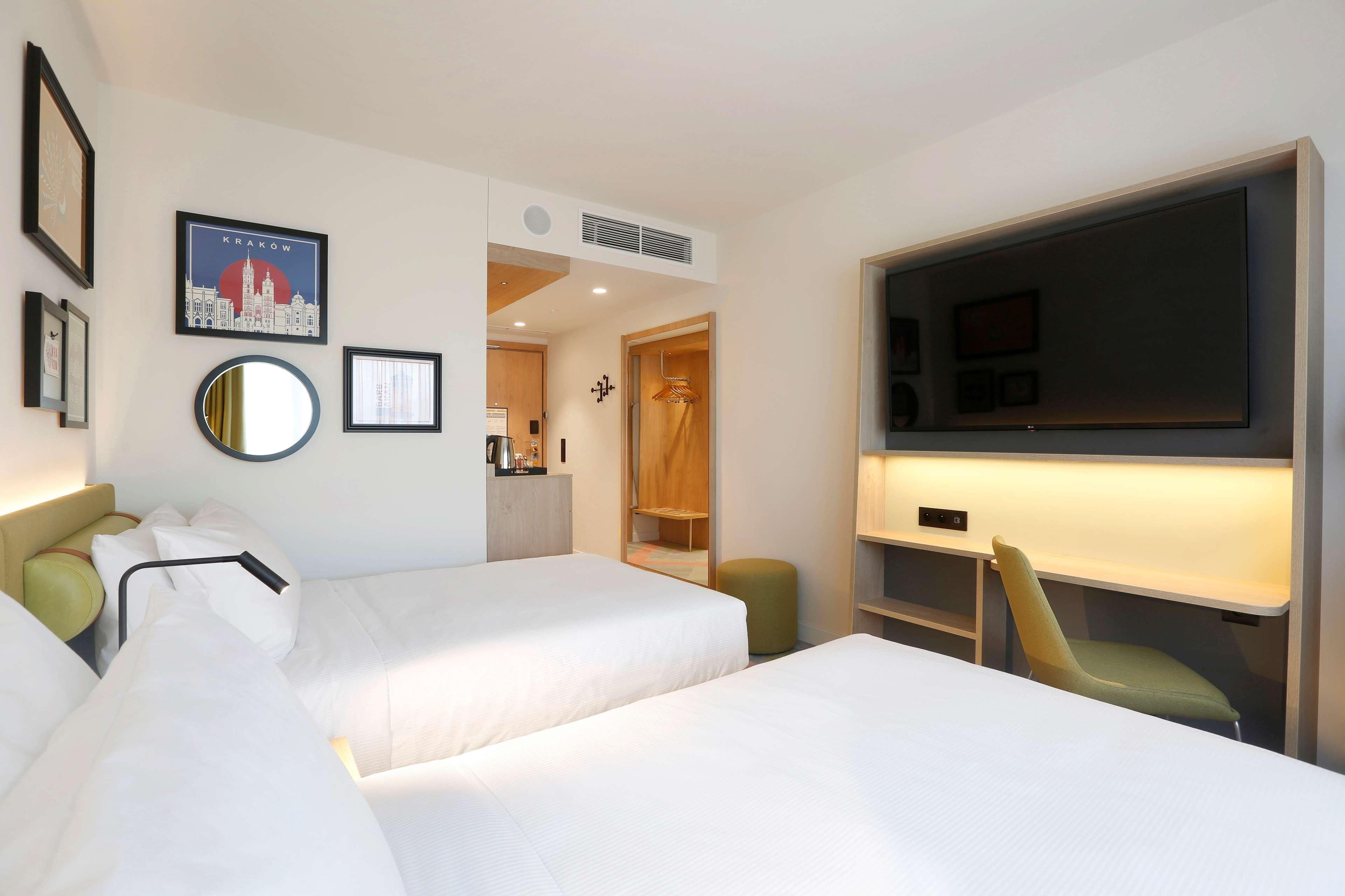 A hotel room with two beds, a TV, a mirror, and a cityscape picture on the wall.