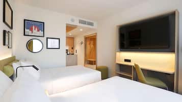 A hotel room with two beds, a TV, a mirror, and a cityscape picture on the wall.