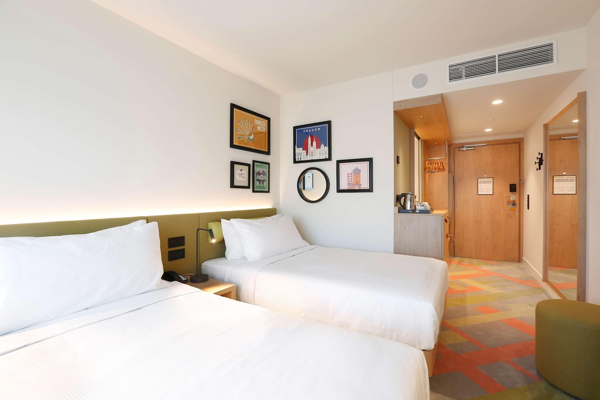A hotel room with two beds, a nightstand, a mirror, and a framed picture on the wall.