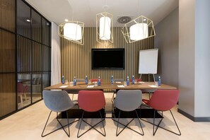 A conference room with a long table, four chairs, a flat-screen TV, a whiteboard, and three pendant lights. - Hampton By Hilton Krakow Airport (Zabierzow)