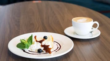 A dessert plate with whipped cream, blueberries, and chocolate sauce on a white plate, accompanied by a cup of coffee on a saucer.