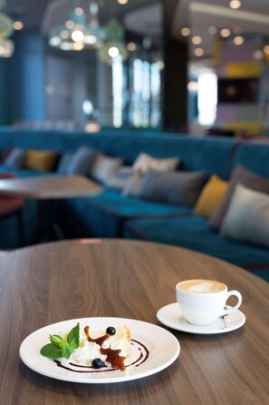 A dessert plate with whipped cream, blueberries, and chocolate sauce on a white plate, accompanied by a cup of coffee on a saucer. - Hampton By Hilton Krakow Airport (Zabierzow)