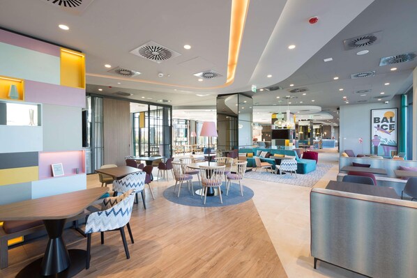 A modern interior with a central dining area, seating arrangements, and a visible bar area. - Hampton By Hilton Krakow Airport (Zabierzow)