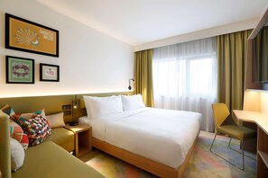 Una habitación de hotel con una cama, un escritorio, una silla, una mesita de noche y una pared decorada con cuadros.