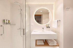 A modern bathroom with a glass-enclosed shower, a white sink with a mirror, and a towel rack. - Hampton By Hilton Krakow Airport (Zabierzow)