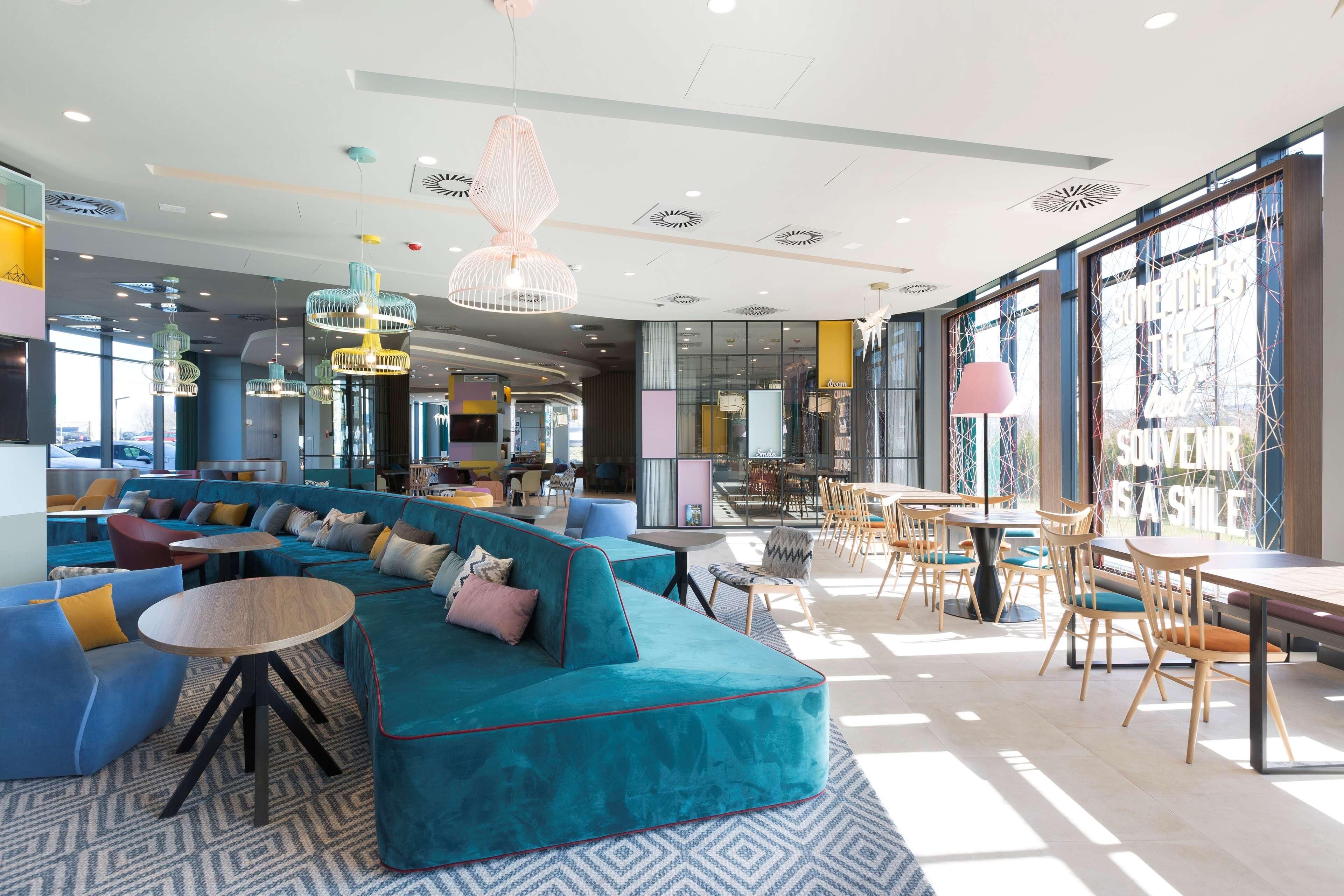 Un espace de détente moderne avec un canapé turquoise, des tables rondes et des lampes suspendues.