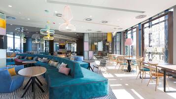A modern lounge area with a teal sofa, round tables, and hanging pendant lights.