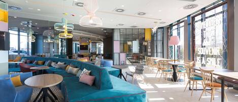 Un espace de détente moderne avec un canapé turquoise, des tables rondes et des lampes suspendues.