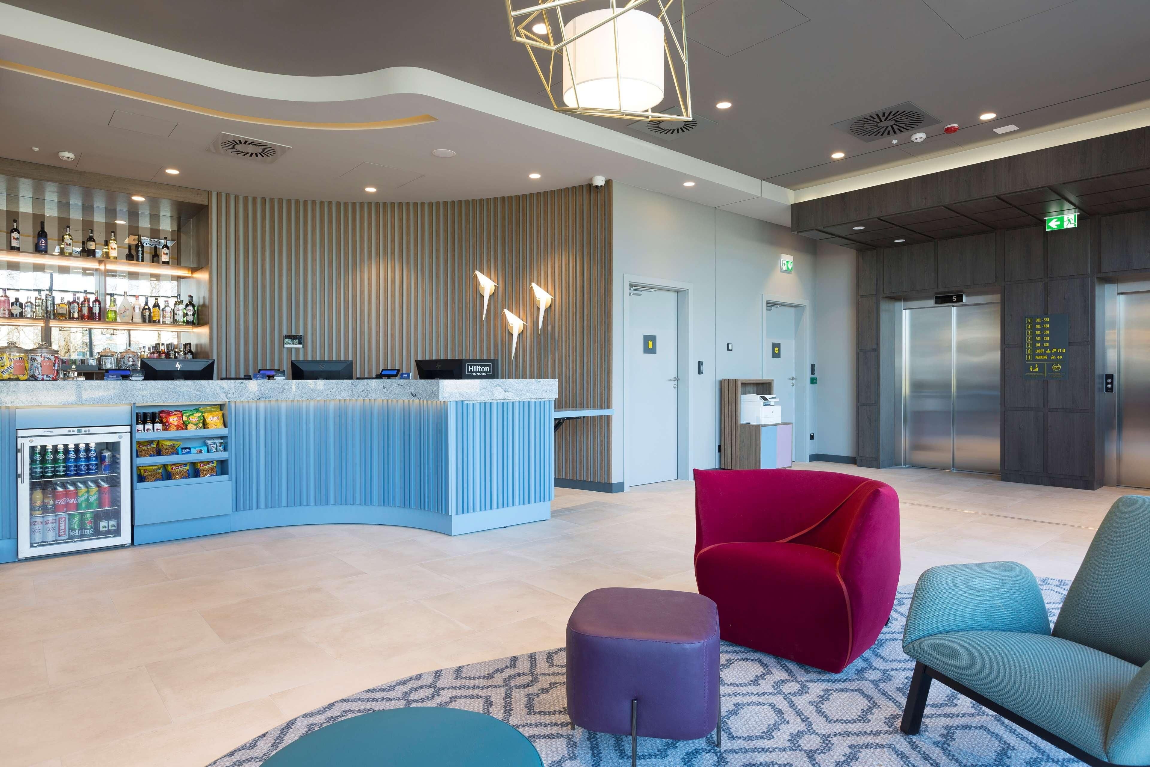 A modern hotel lobby with a bar area, seating, and an elevator.