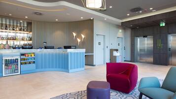 A modern hotel lobby with a bar area, seating, and an elevator.
