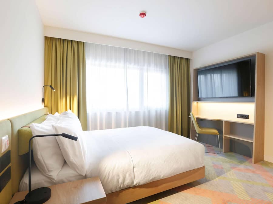 A hotel room with a bed, a desk, a chair, a television, and a window with curtains.