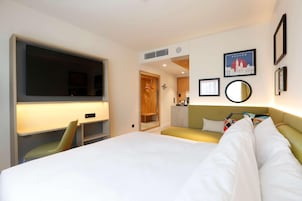 Habitación de hotel con cama, escritorio, silla, televisor, armario y espejo.