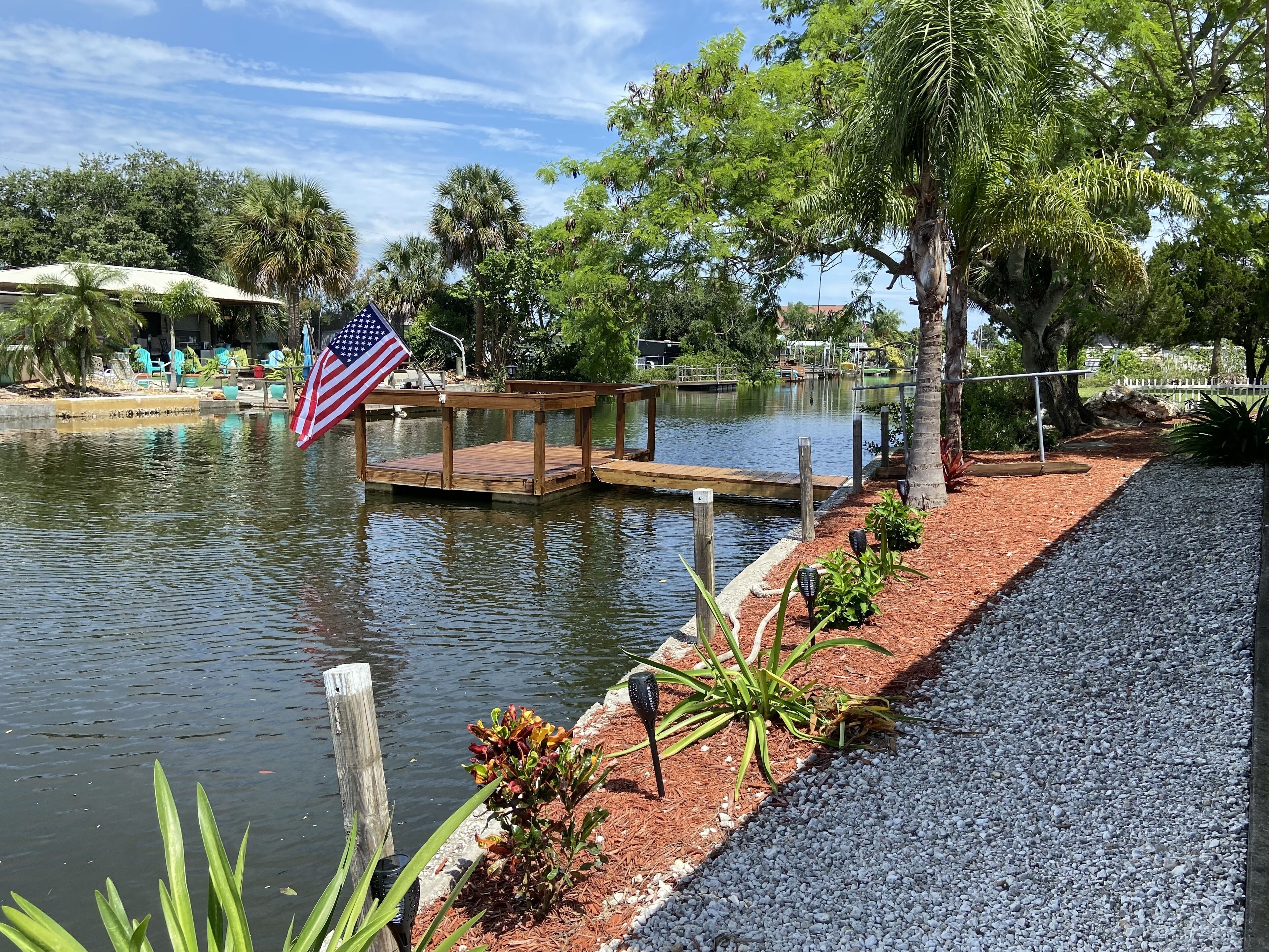 Un cadre paisible au bord d’un lac, avec une jetée en bois, un drapeau américain et un jardin bien entretenu.