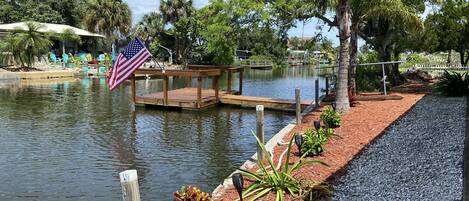 Un cadre paisible au bord d’un lac, avec une jetée en bois, un drapeau américain et un jardin bien entretenu.