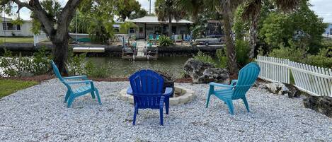 A patio area with three blue Adirondack chairs, a small table, and a pathway leading to a dock over water.