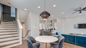 Una cocina moderna con una isla central, un rincón comedor con dos sillas y una escalera de madera.