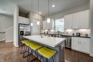 Une cuisine moderne avec des meubles blancs, des appareils en acier inoxydable et un îlot central doté de tabourets de bar.