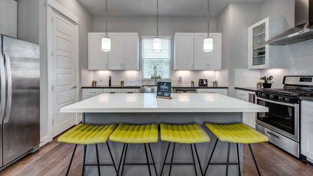 Una cocina moderna con una isla central, taburetes de bar, electrodomésticos de acero inoxidable e iluminación colgante.