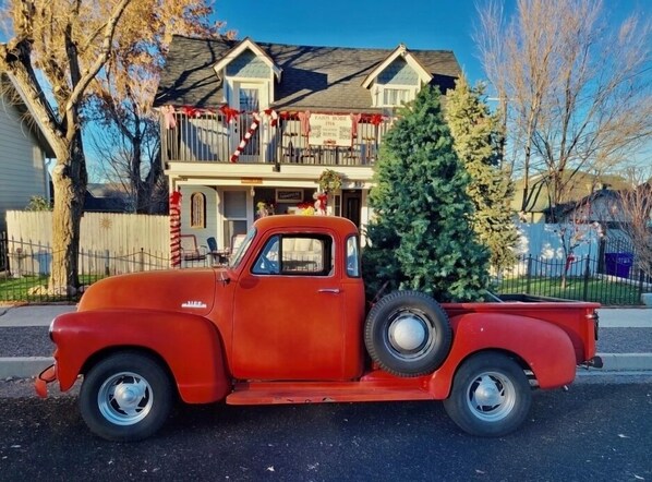 A vintage red truck parked in front of a house with a Christmas tree in the bed.