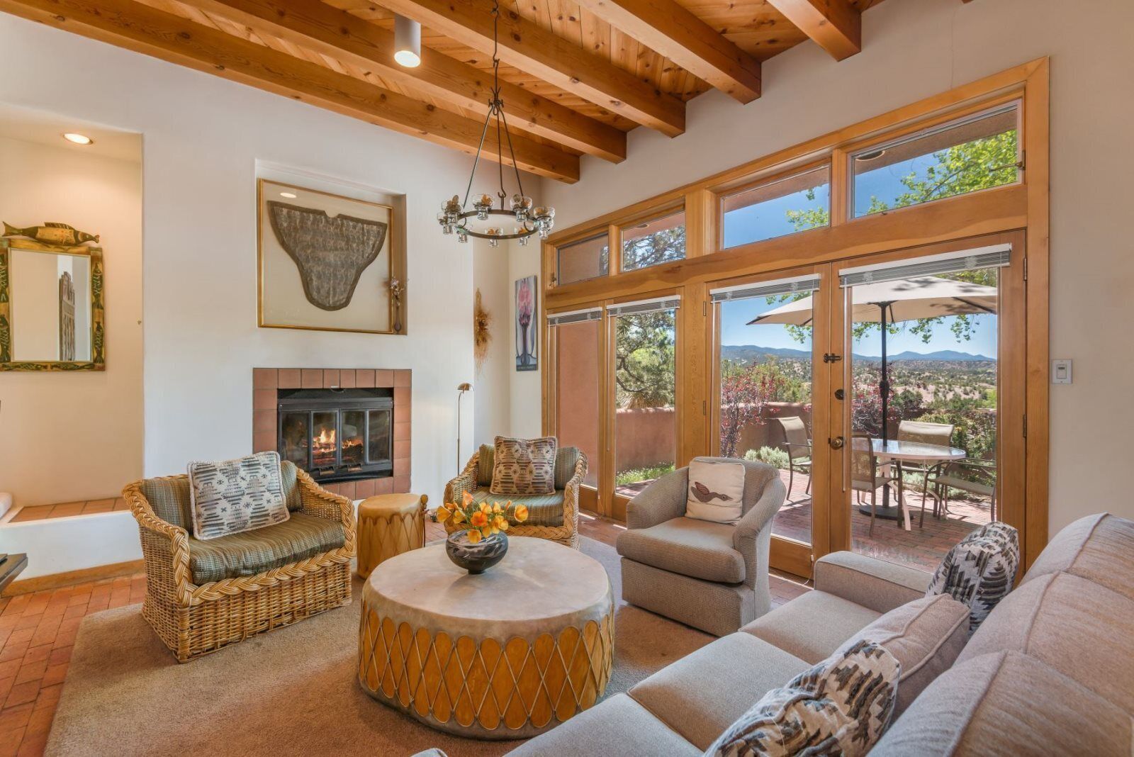 Un salón amplio con chimenea, muebles de mimbre y ventanas grandes que ofrecen vistas al exterior.