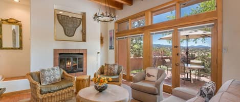 Un salón amplio con chimenea, muebles de mimbre y ventanas grandes que ofrecen vistas al exterior.