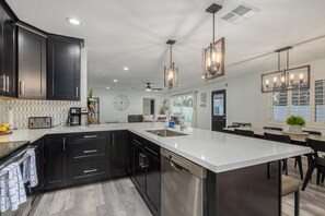 Une cuisine moderne avec des meubles de couleur sombre, un grand îlot central et des luminaires suspendus.