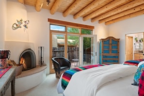 A cozy bedroom with a fireplace, a large bed, a wooden wardrobe, and a sliding glass door leading to an outdoor area.