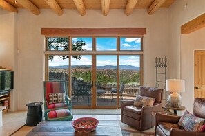 A spacious living room with a large sliding glass door leading to an outdoor patio. Inside, there is a leather sofa, a television, and a woven basket on a wooden table.
