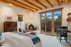 A cozy bedroom with a fireplace, a large bed, a desk, and a view of the outdoors. - Casa Serena - Breathtaking and Peaceful Views From Swimming Pool (Santa Fe)